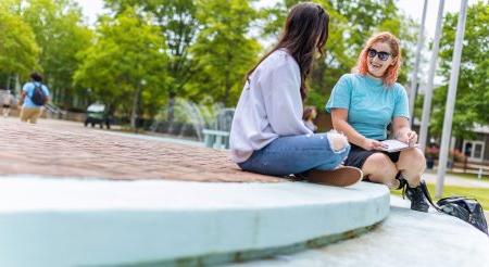 Two female students are sitting on the steps in front of the Webb center talking